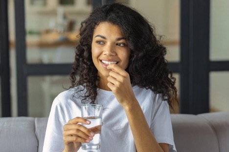 A woman takes prescribed medication for bowel preparation, holding a glass of water and medicine