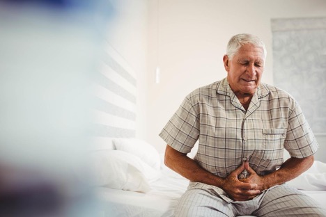 An elderly man in the bedroom is clutching his stomach, experiencing the pain of colon cancer.